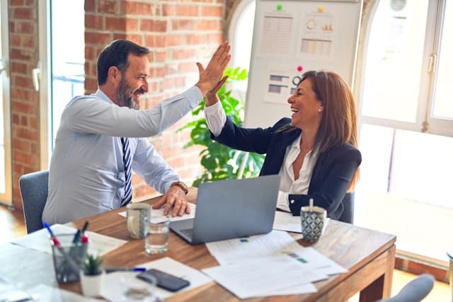 A businessman and businesswoman high-five after successfully completing an organizational cultural assessment